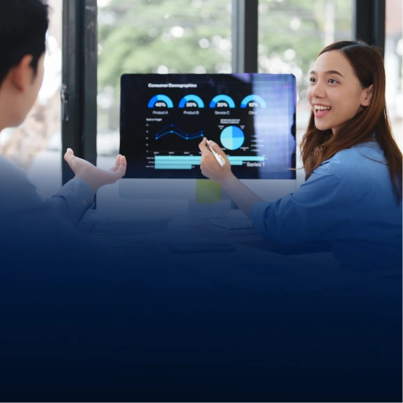 Two professionals reviewing consumer demographics charts on a large monitor