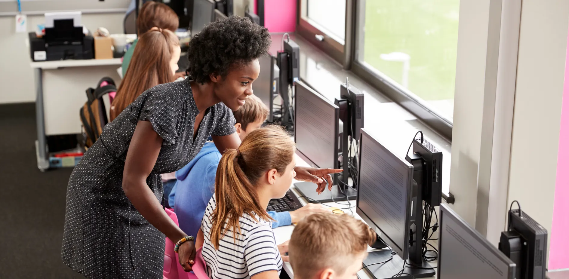 Teacher guiding students in a school computer lab