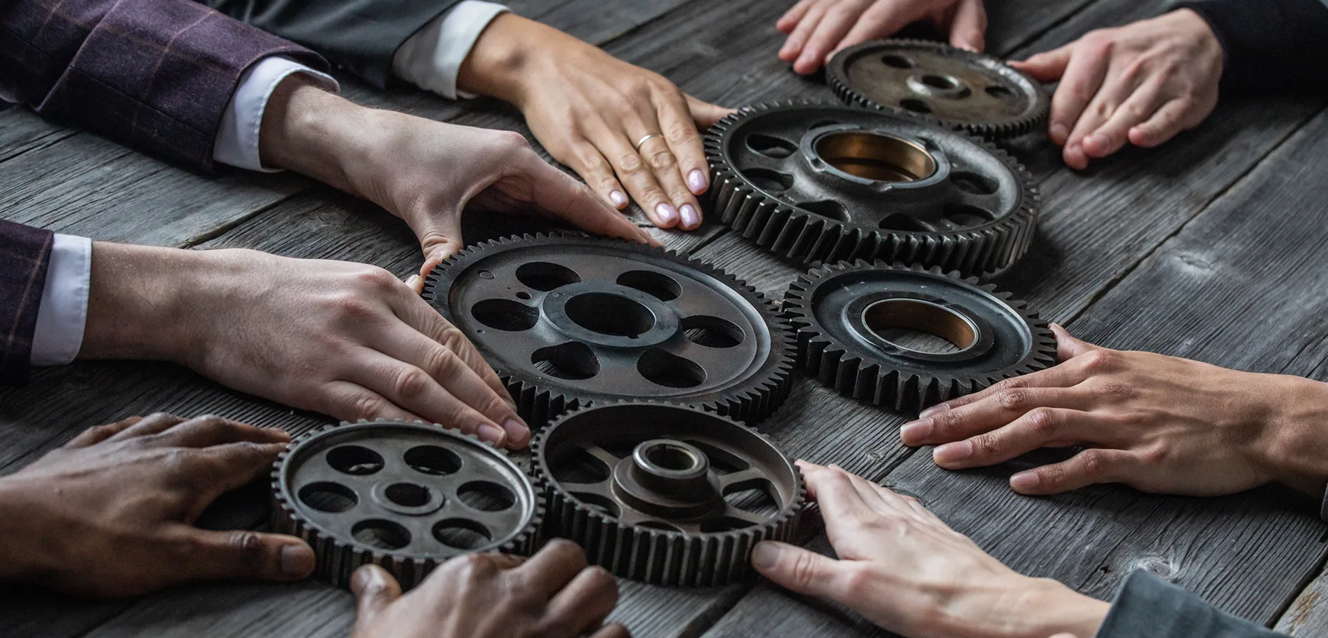 Hands of a business team fitting metal gears together on a wooden table