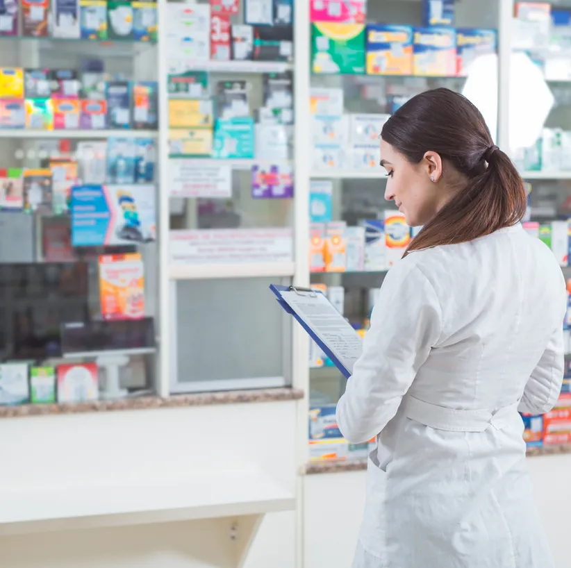 Pharmacist with a clipboard checking medicine shelves